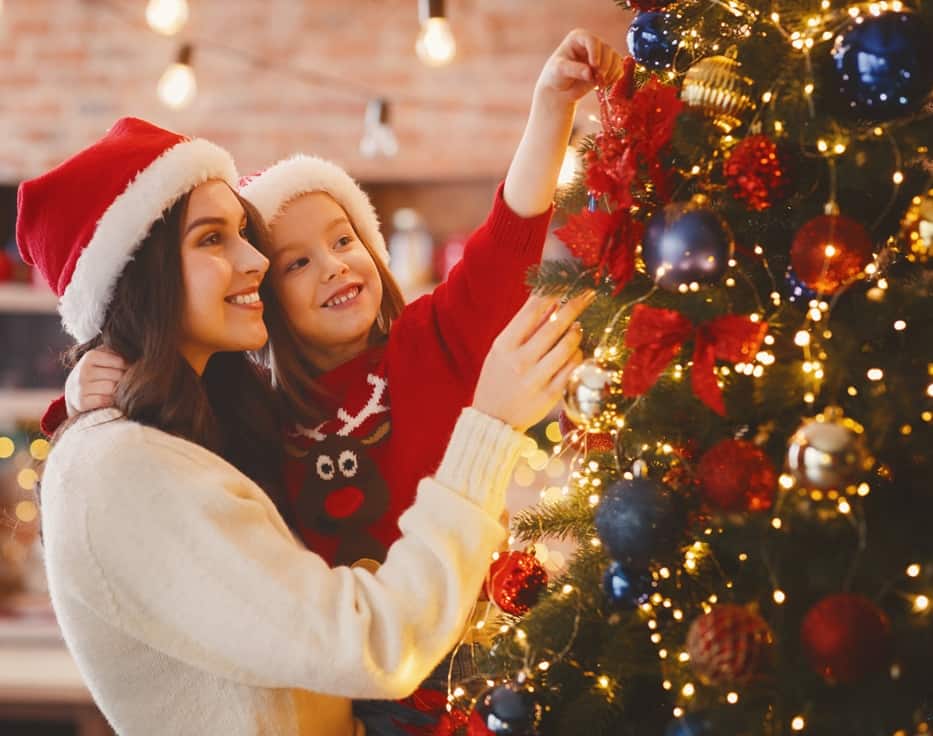 Festive mother and daughter decorating Christmas tree at home