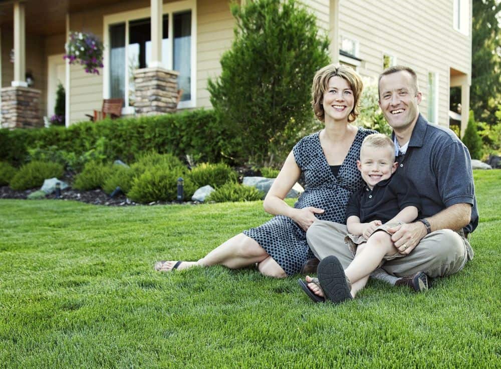 smiling family sits on their front lawn