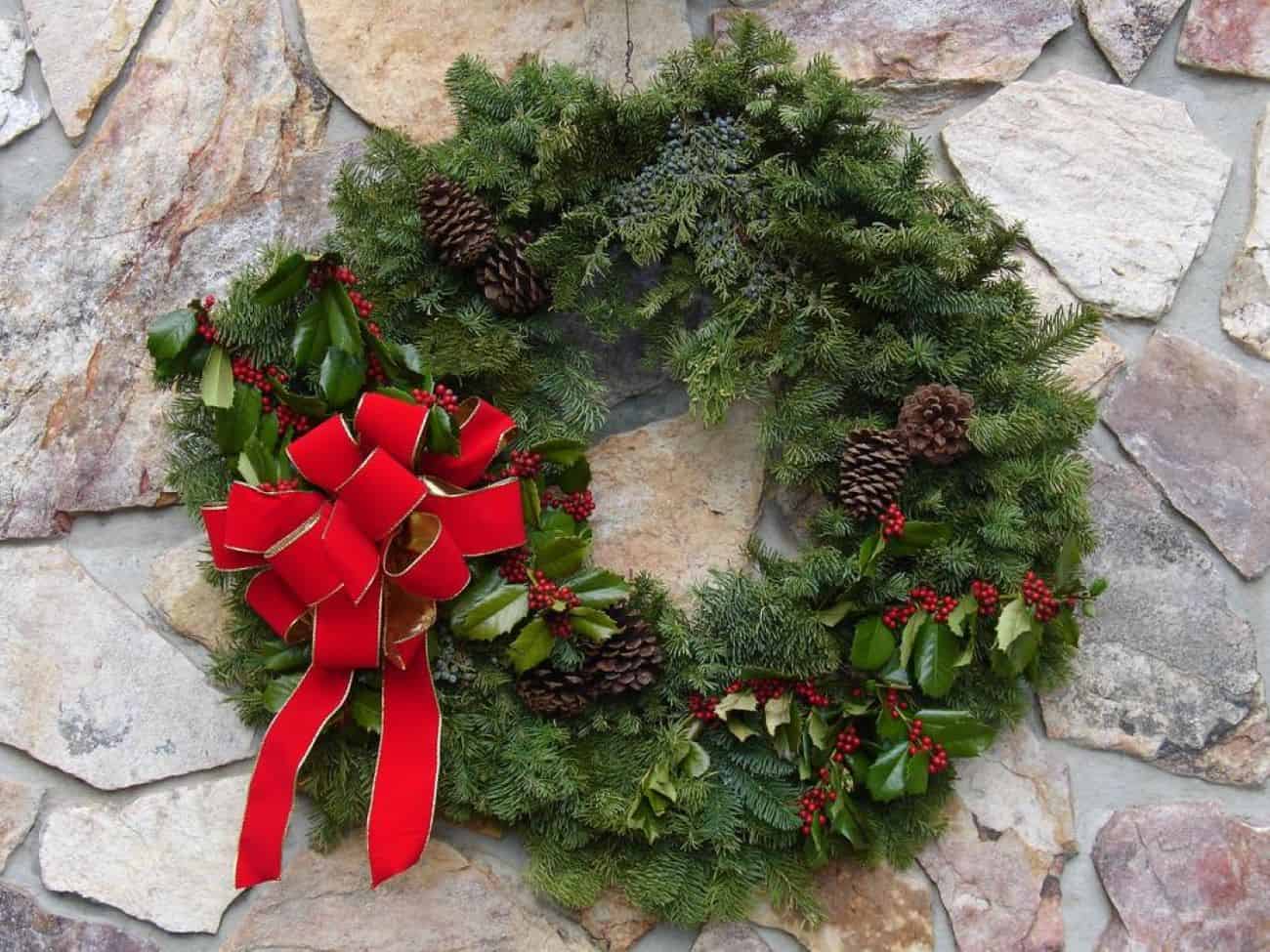 an evergreen holiday wreath with a red ribbon and pine cones
