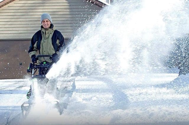 a man removes snow from a driveway with a cordless electric snow blower