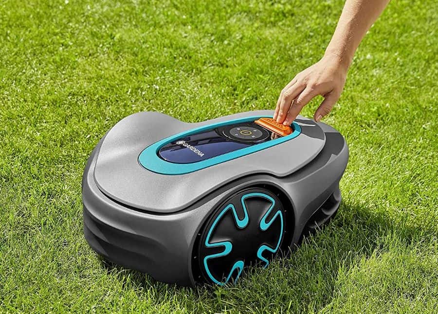a hand touching a Gardena robotic lawn mower that is sitting on a grass lawn