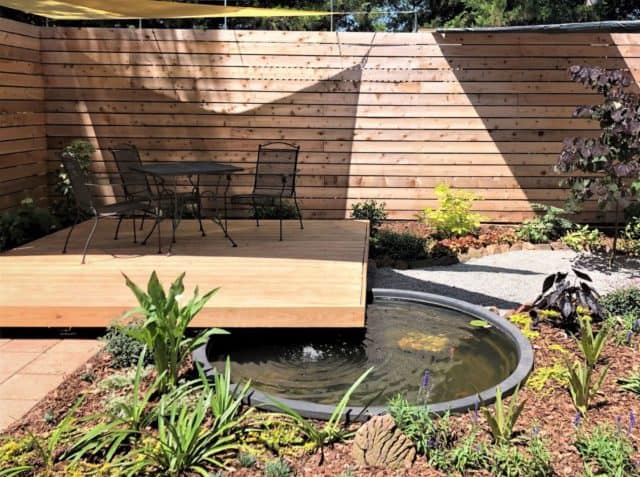 a floating deck in a backyard with plants and a pond