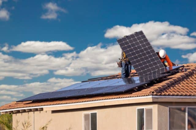 workers install solar panels on the roof of a house