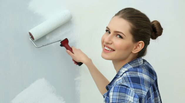 a woman paints a bedroom wall with a paint roller