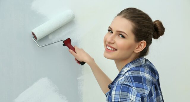 a woman paints a bedroom wall with a paint roller